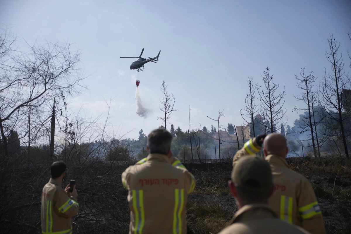 Israeli firefighters watch a helicopter drop water on a wildfire next to a monastery in Latrun, Israel, outside of Jerusalem, Thursday, May 1, 2025. (AP Photo/Ohad Zwigenberg)