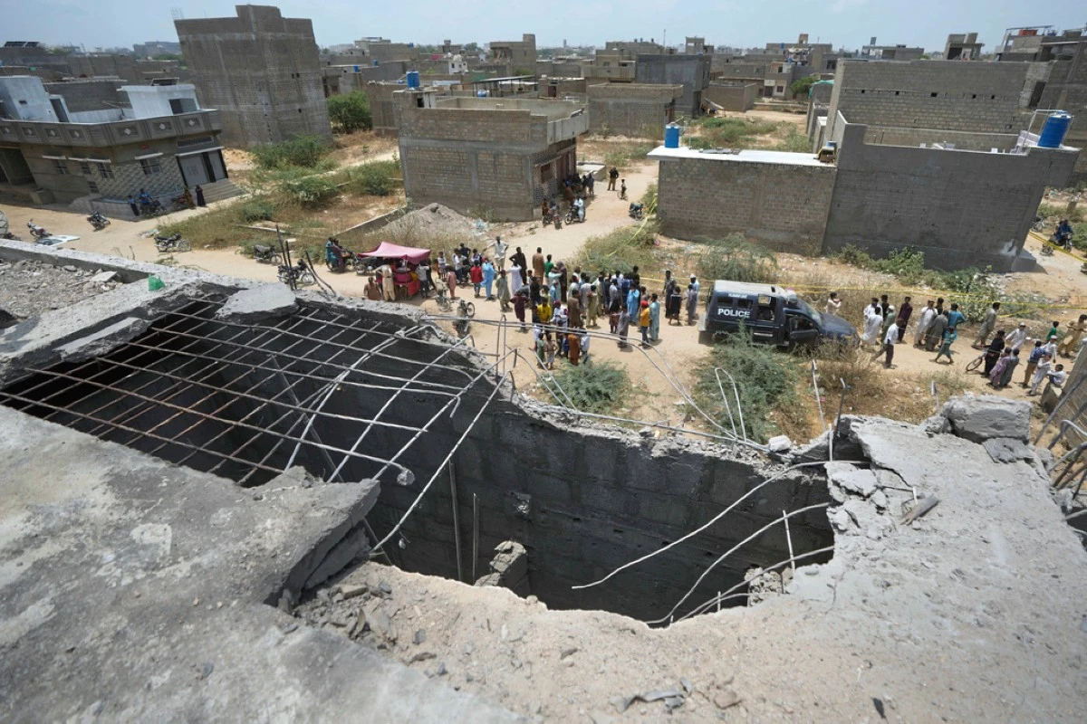 A big hole is seen on a rooftop of a house suspected to have been damaged in Indian drone attack as
residents, behind, gather near a cordoned off site, where Pakistan's air defense system shot down a suspected Indian drone in Karachi, Pakistan, Thursday, May 8, 2025. (AP Photo/Fareed Khan)