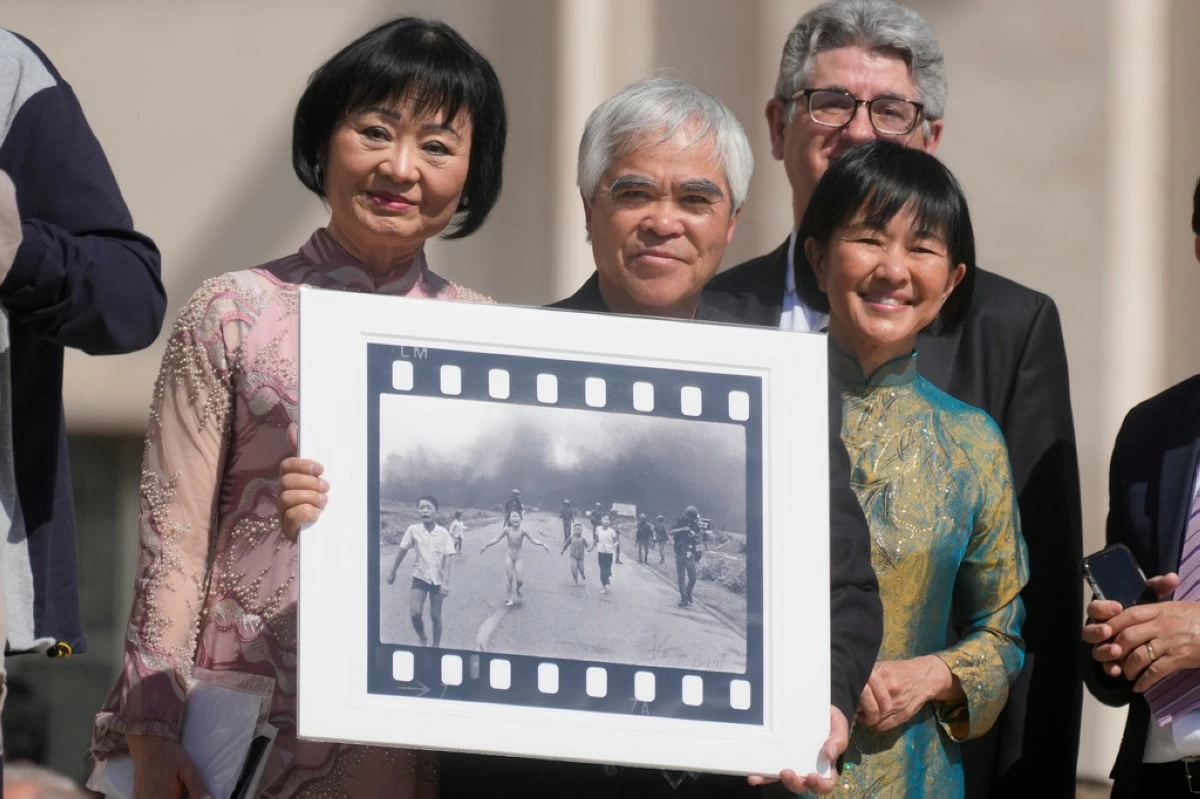 FILE - Pulitzer Prize-winning photographer Nick Ut, center, flanked by Kim Phuc, left, holds the" Napalm Girl", his Pulitzer Prize winning photo as they wait to meet with Pope Francis during the weekly general audience in St. Peter's Square at The Vatican, May 11, 2022. (AP Photo/Gregorio Borgia, file)