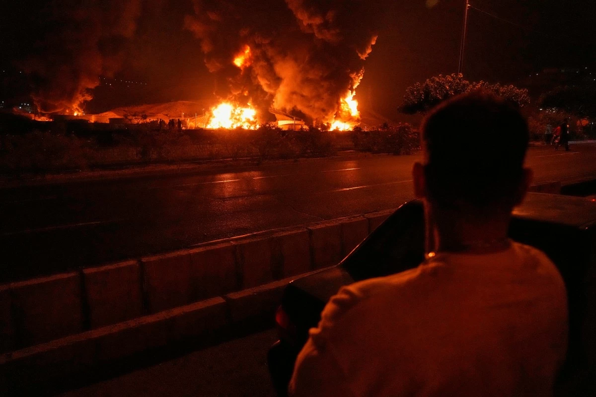 A man looks at flames rising from an oil storage facility after it appeared to have been struck by an Israeli strike in Tehran, Iran, early Sunday, June 15, 2025. (AP Photo/Vahid Salemi)