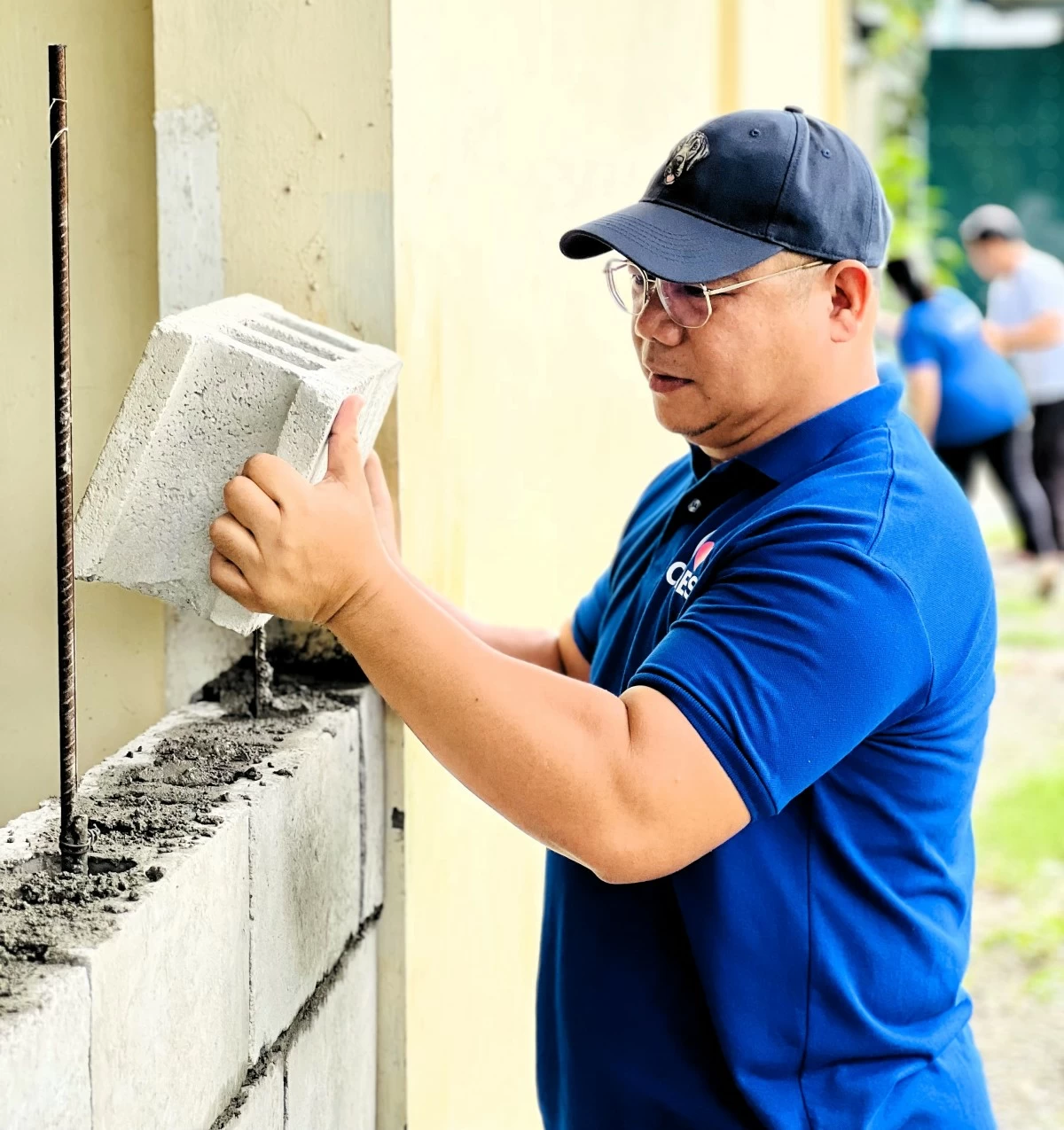Demonstrating hands-on commitment, an employee volunteer from SM City Baliwag carefully stacks hollow blocks—contributing to stronger school infrastructure.