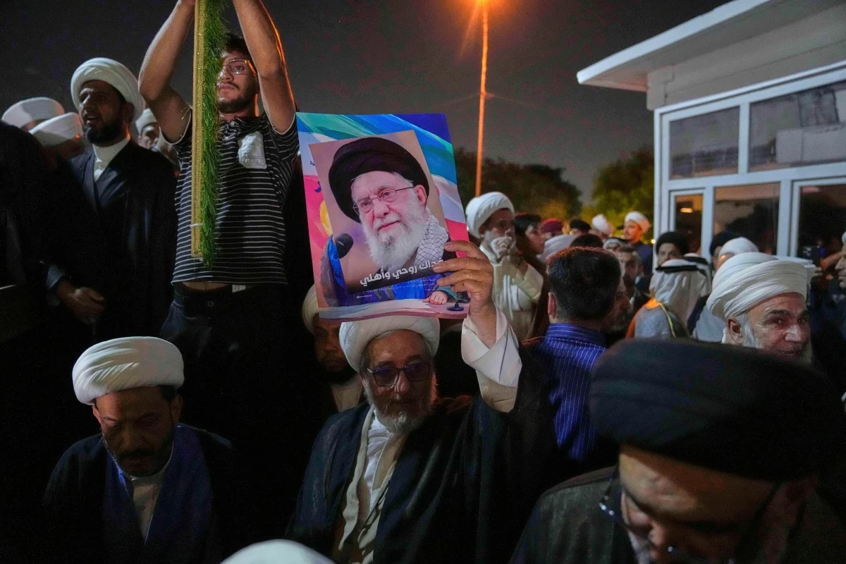 An Iraqi Shiite cleric holds a portrait of Iran's Supreme Leader Ayatollah Ali Khamenei during a protest against Israeli attacks on multiple cities across Iran, at a bridge leading to the fortified Green Zone where the U.S. Embassy is located in Baghdad, Iraq, Thursday, June 19, 2025. (AP Photo/Hadi Mizban)