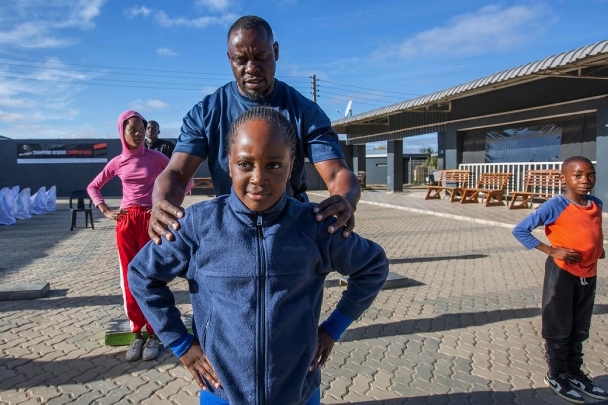 Actions Winya, a yoga instructor assists a young girl in perfecting her pose at Socialite Bar in Chitungwiza on the outskirts of Harare, Zimbabwe, Friday, June 20, 2025. (AP Photo/Aaron Ufumeli)