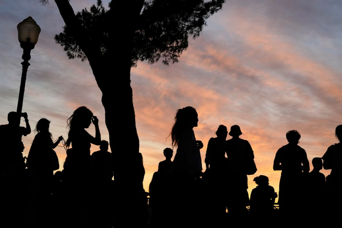 People watch the sun set from the Our Lady of the Hill viewpoint overlooking Lisbon at the end of a hot day in Lisbon, Friday, June 27, 2025. (AP Photo/Armando Franca)