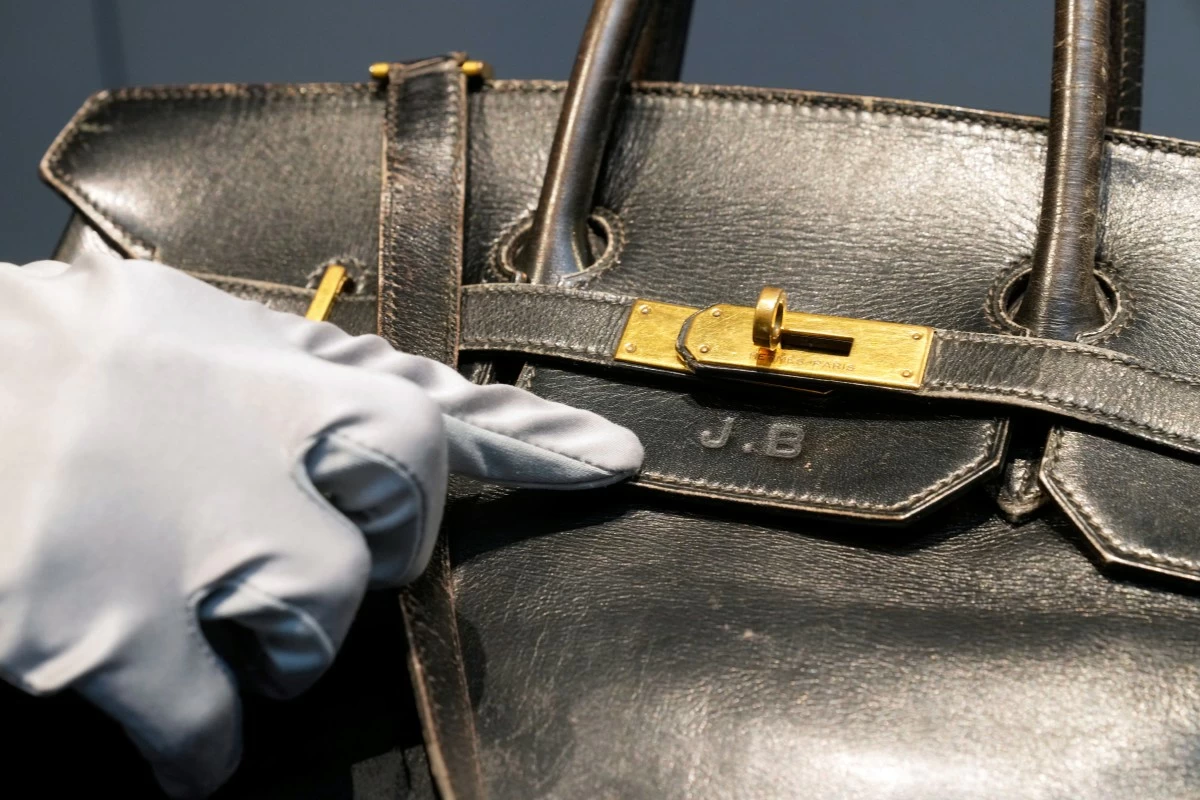 An auction officer points to Jane Birkin's initials on the original Birkin bag created by Hermès for Jane Birkin in 1984, prior to its auction Thursday, July 10, 2025 in Paris. (AP Photo/Michel Euler)
