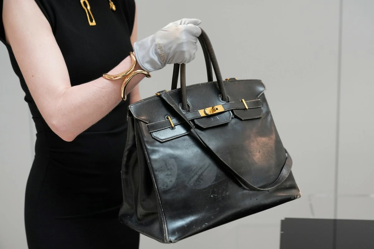 An auction officer carries the original Birkin bag created by Hermès for Jane Birkin in 1984, prior to its auction Thursday, July 10, 2025 in Paris. (AP Photo/Michel Euler)