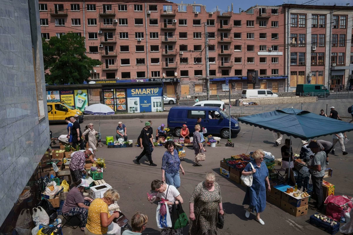 People shop at a street market near a building which was damaged by a Russian attack in Kyiv, Ukraine, on Thursday, July 10, 2025. (AP Photo/Evgeniy Maloletka)