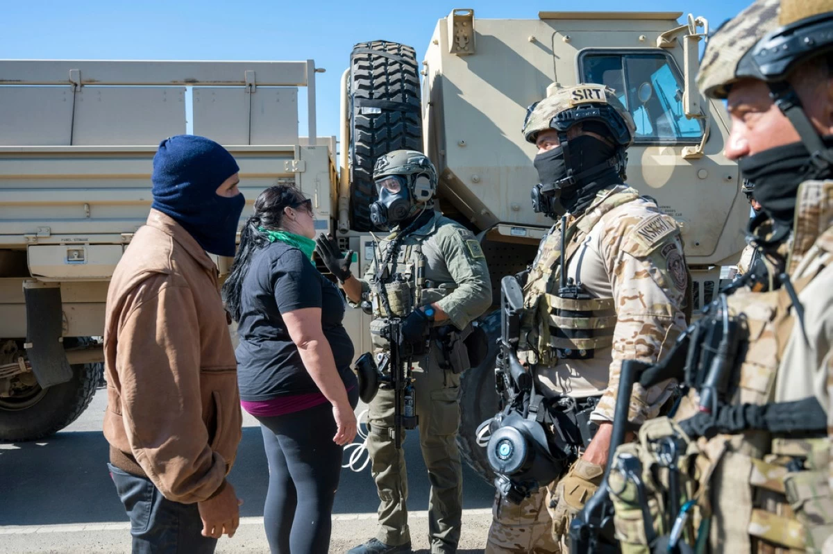Federal immigration agents talk to Rebecca Torres, second left, after she tried to block a military vehicle during a raid in the agriculture area of Camarillo, Calif., Thursday, July 10, 2025. (AP Photo/Michael Owen Baker)