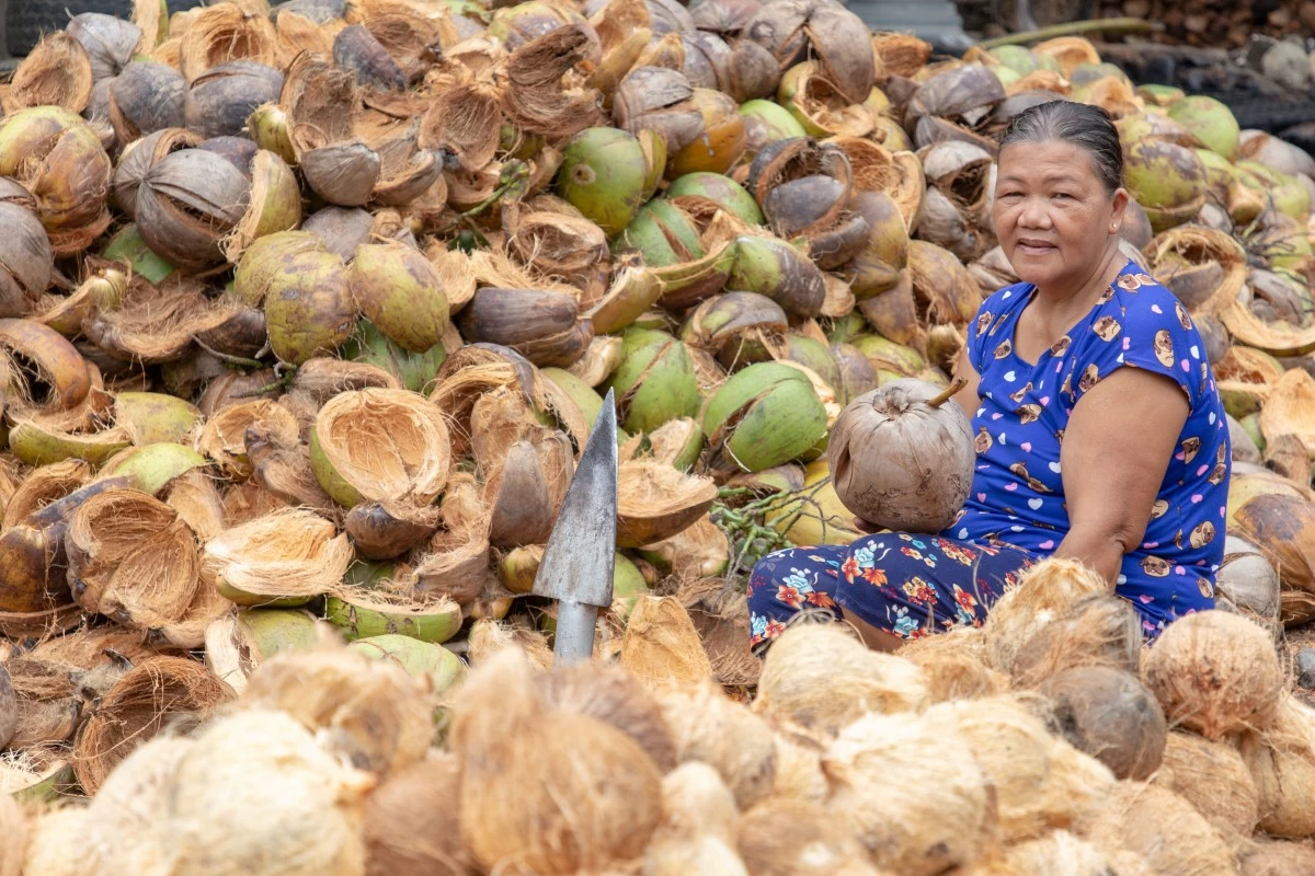 A resilient Nanay member sits among the fruits of her labor in her coconut processing business. With the support of ASA Philippines, her entrepreneurial spirit not only provides her with income but also enables her to invest in her family's well-being and build a more secure future.