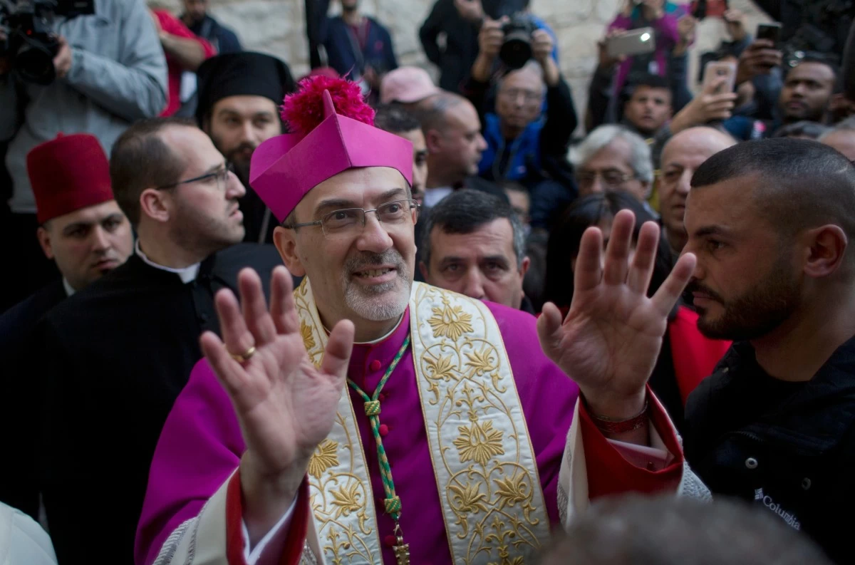FILE- In this Dec. 24, 2018 file photo, Christians celebrate the arrival of Archbishop Pierbattista Pizzaballa, the top Roman Catholic cleric in the Holy Land, center, after he crossed an Israeli military checkpoint from Jerusalem ahead of midnight Mass at the Church of the Nativity, traditionally recognized by Christians to be the birthplace of Jesus Christ, in the West Bank city of Bethlehem. (AP Photo/Nasser Nasser, File)