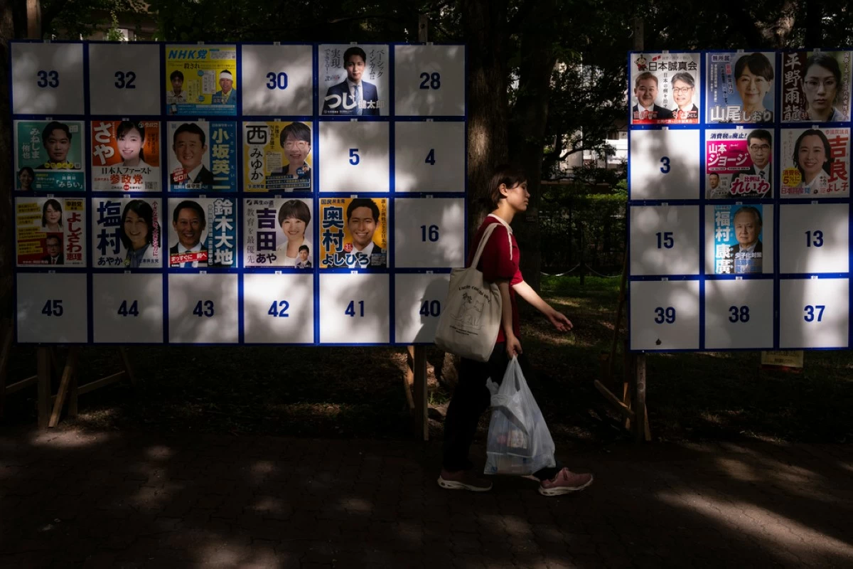 A pedestrian passes an election board displaying posters of candidates for the upcoming July 20 upper house election in Tokyo, Friday, July 18, 2025. (AP Photo/Louise Delmotte)