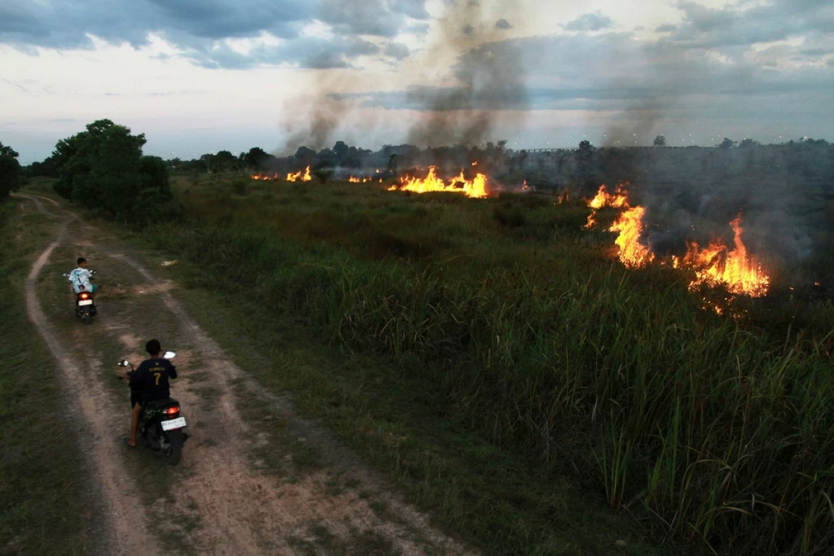 Motorists ride past a fire that razes through a peatland field in Ogan Ilir, South Sumatra, Indonesia, Sunday, July 20, 2025. (AP Photo/Muhammad Hatta)