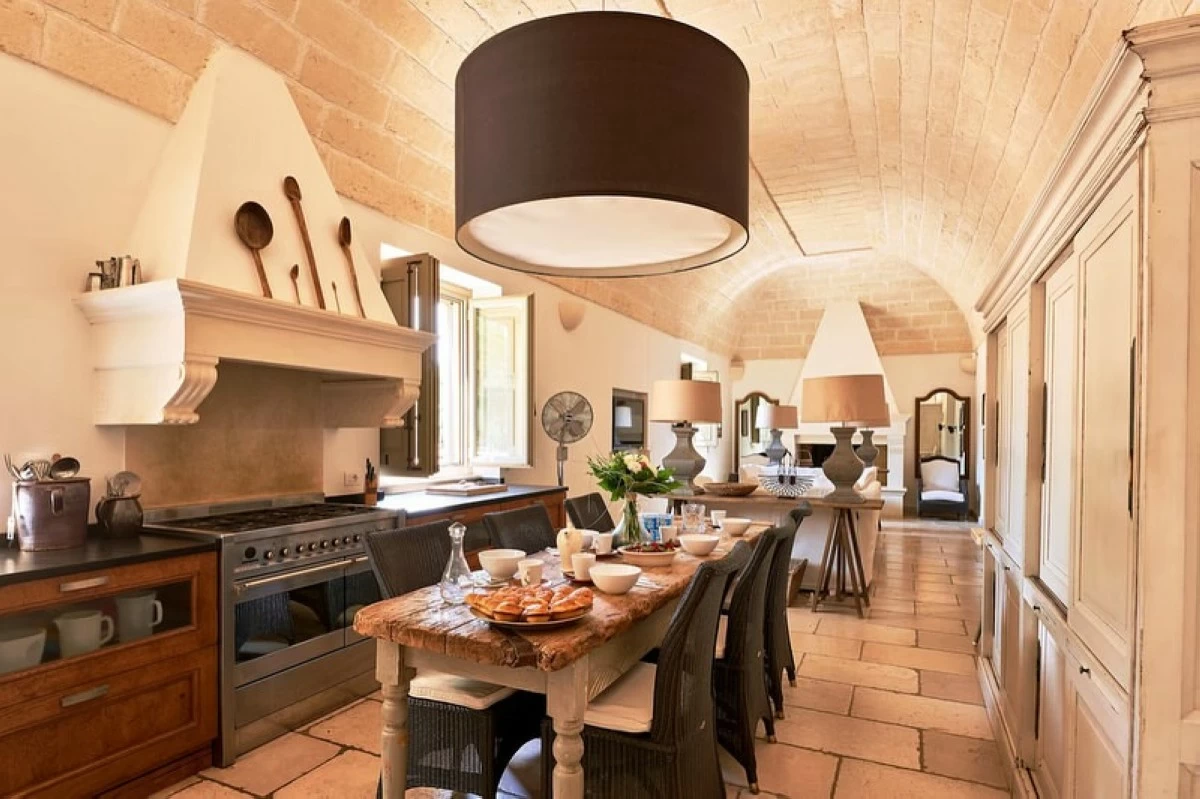 The dining area has brick accents, wide windows, and a drum-shaped light, with wood, black, and ceramic details matching the pale stone walls.