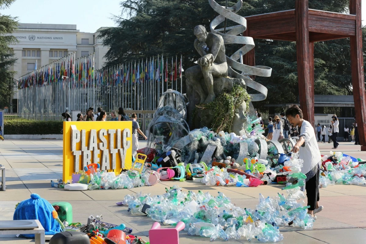 Benjamin Von Wong, right, a Canadian artist and activist, heaps piles of plastic waste onto a large sculpture that he designed in front of the United Nations office in Geneva, Switzerland, Monday, Aug. 11, 2025. (AP Photo/ Jennifer McDermott)