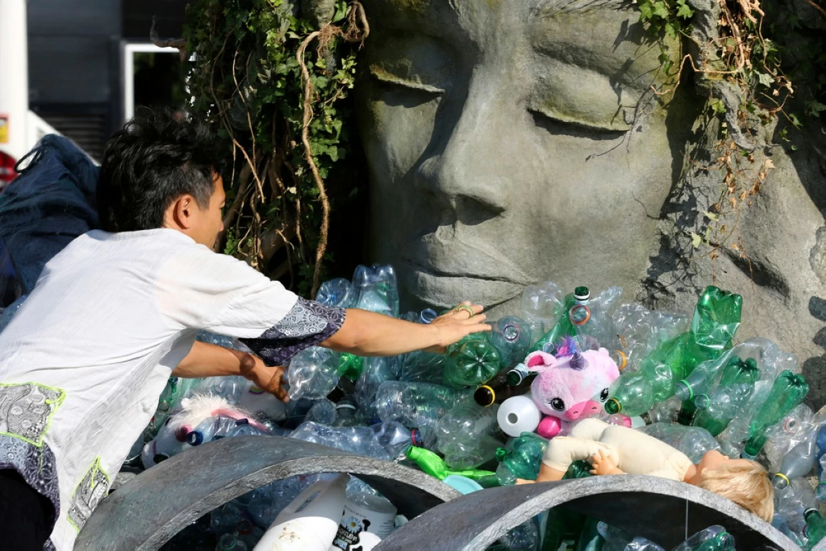 Benjamin Von Wong, a Canadian artist and activist, heaps piles of plastic waste onto a large sculpture that he designed in front of the United Nations office in Geneva, Switzerland, Monday, Aug. 11, 2025. (AP Photo/ Jennifer McDermott)