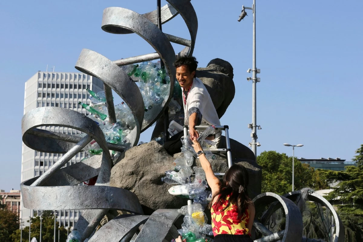 Benjamin Von Wong, top, a Canadian artist and activist, heaps piles of plastic waste onto a large sculpture that he designed in front of the United Nations office in Geneva, Switzerland, Monday, Aug. 11, 2025. (AP Photo/ Jennifer McDermott)