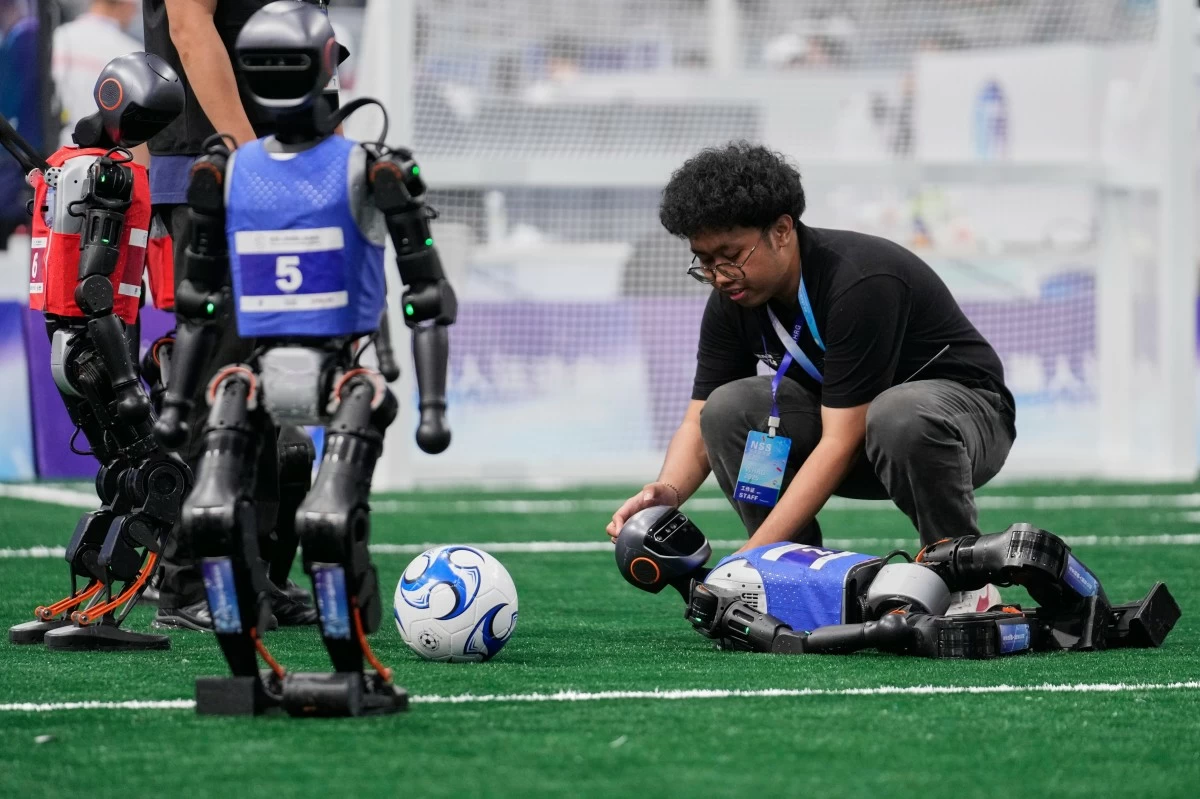 A technician assists a robot that fell during a soccer match at the World Humanoid Robot Games in Beijing, China, Friday, Aug. 15, 2025. (AP Photo/Mahesh Kumar A.)