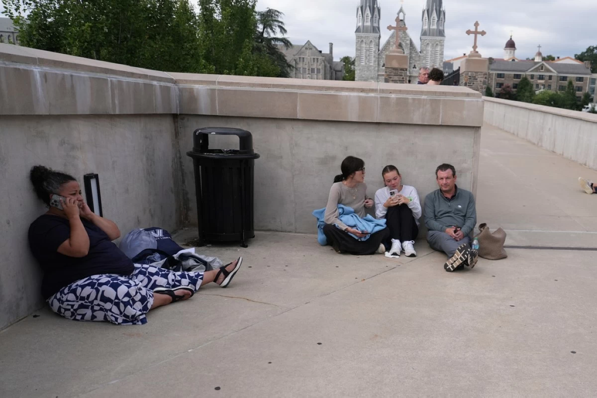 People shelter behind a wall on the Villanova University campus in Villanova, Pa., on Thursday, Aug. 21, 2025, where an active shooter was reported. (AP Photo/Matt Slocum)
