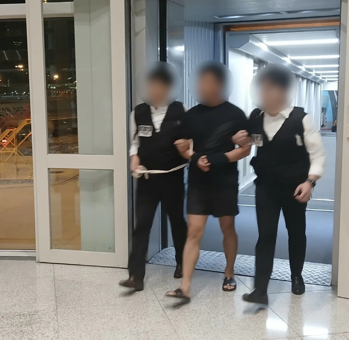 The leader of a hacking organization (center) is escorted by the police as he arrives at Incheon International Airport on Aug. 22 (Korea's Ministry of Justice)