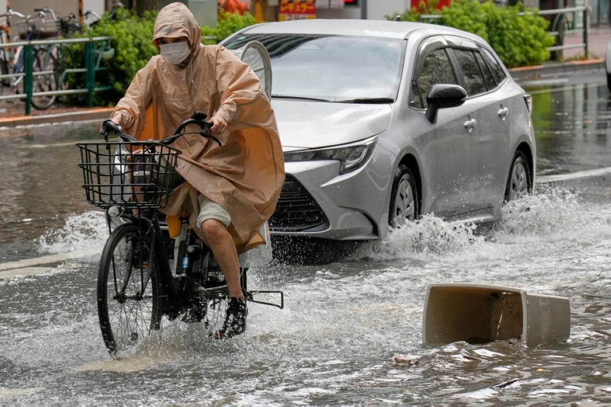 A person rides a bicycle through a flooded road caused by heavy rain Thursday, Sept. 11, 2025, in Tokyo. (AP Photo/Eugene Hoshiko)