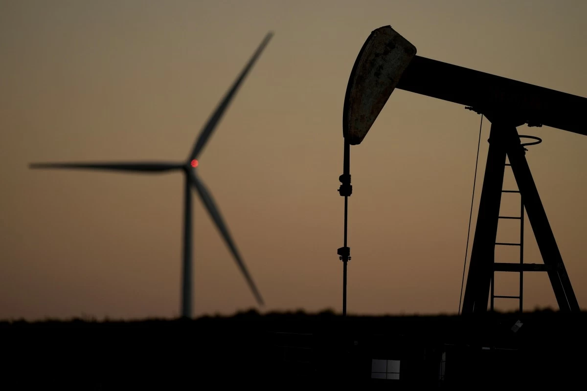 A pumpjack operates in the foreground while a wind turbine at the Buckeye Wind Energy wind farm rises in the distance, Sept. 30, 2024, near Hays, Kan. (AP Photo/Charlie Riedel, File)