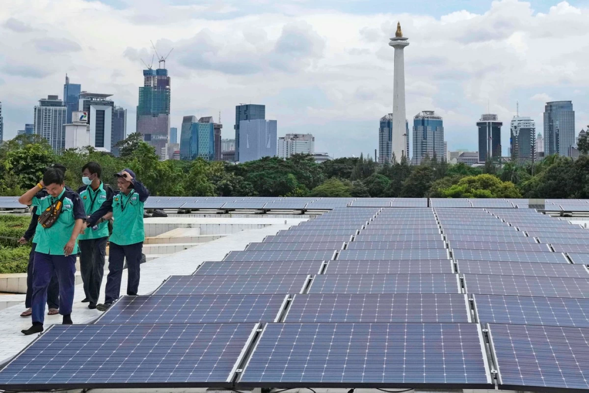 FILE - Workers walk near solar panels that provide partial electrical power to Istiqlal Mosque as the city skyline is seen in the background, in Jakarta, Indonesia, Wednesday, March 29, 2023. (AP Photo/Tatan Syuflana, File)