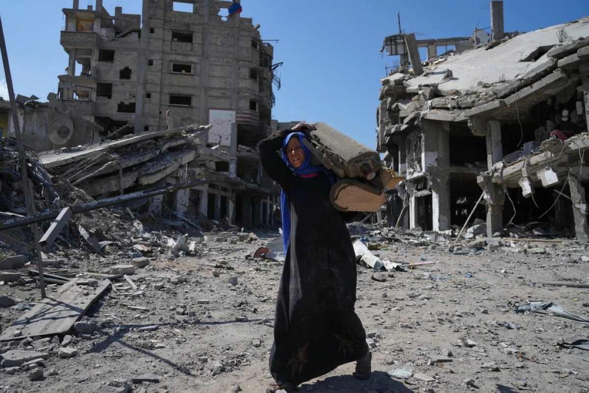 An elderly displaced Palestinian woman carries an item past destroyed buildings in Khan Younis, southern Gaza Strip, Friday, Oct. 10, 2025, after Israel and Hamas agreed to a pause in their war and the release of the remaining hostages. (AP Photo/Jehad Alshrafi)