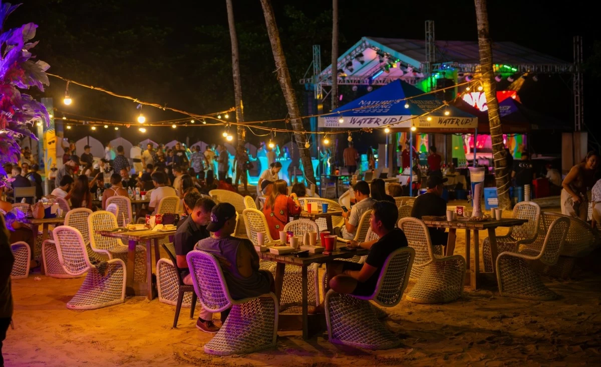 COASTAL GROOVE Guests unwind by the shore as music, lights, and island flavors set the mood for a laid-back Oktoberfest evening