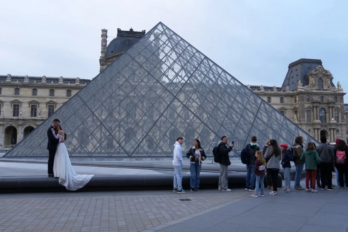 A wedding couple hugs as visitors queue to enter the Louvre museum three days after historic jewels were stolen in a daring daylight heist, Wednesday, Oct. 22, 2025 in Paris. (AP Photo/Thibault Camus)
