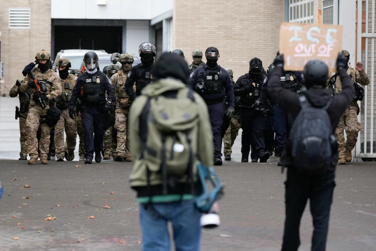 FILE - People protest outside a U.S. Immigration and Customs Enforcement facility as law enforcement officers walk out of the gates to guard vehicles leaving the facility on Oct. 11, 2025, in Portland, Ore. (AP Photo/Jenny Kane, File)