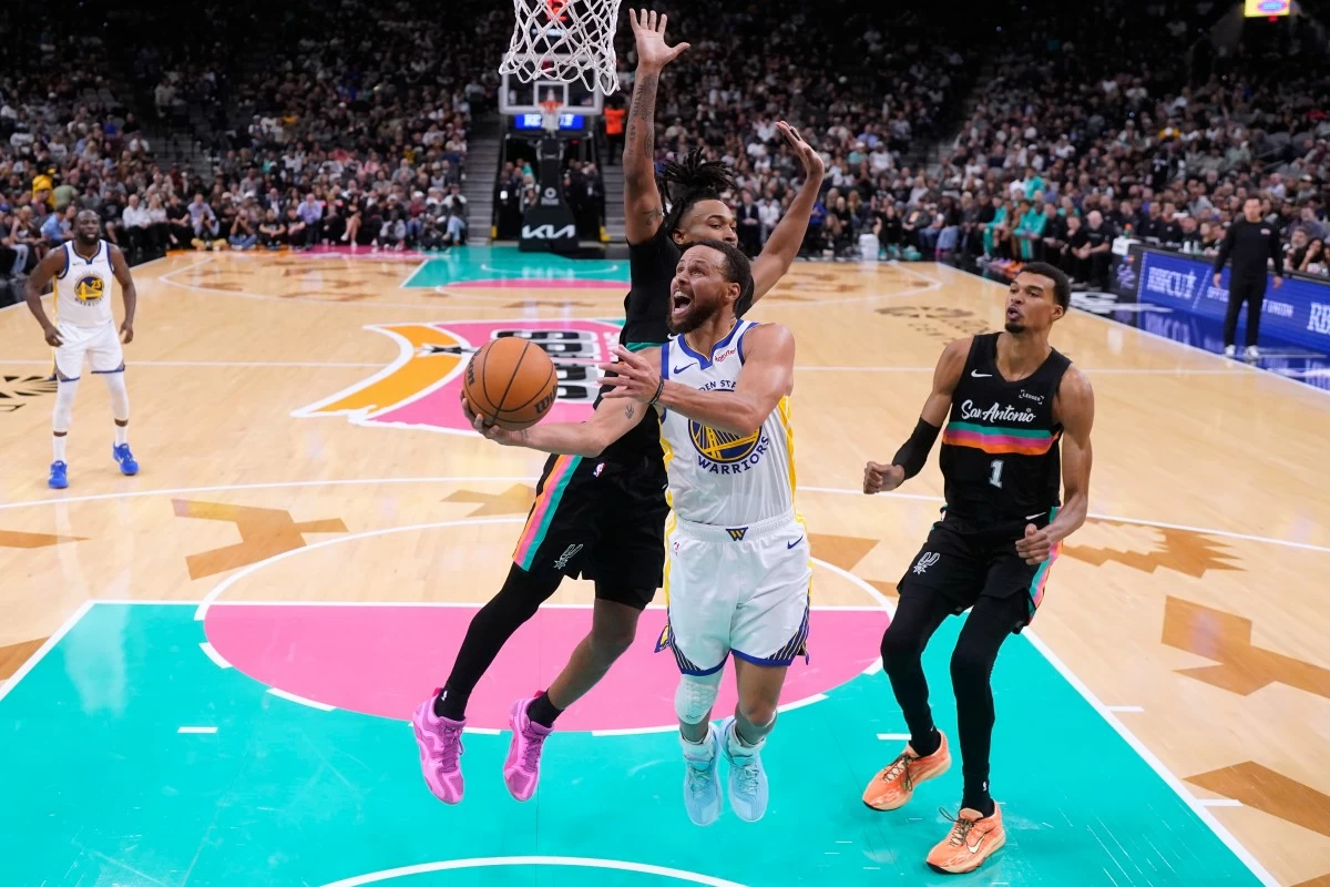 Golden State Warriors guard Stephen Curry (30) drives to the basket past San Antonio Spurs guard Stephon Castle, center, and forward Victor Wembanyama (1) during the second half of an NBA basketball game in San Antonio, Wednesday, Nov. 12, 2025. (AP Photo/Eric Gay)