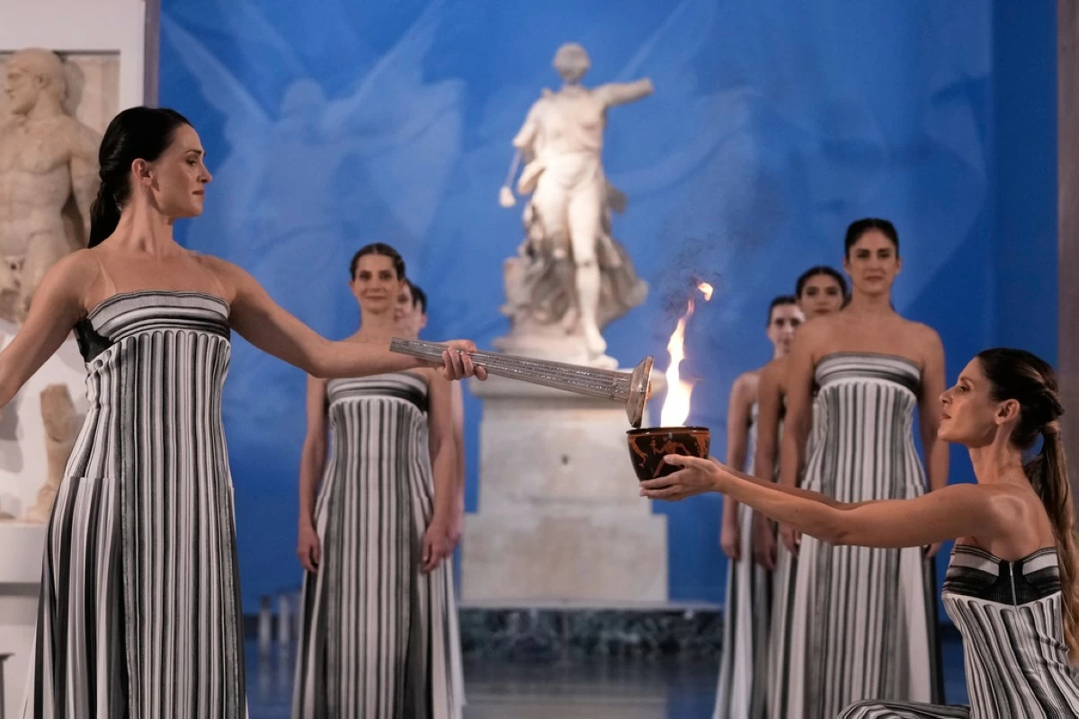 High Priestess Mary Mina, left, lights a torch from the Olympic flame during the flame lighting ceremony for the Milan Cortina 2026 Winter Olympics, at the archaeological museum of Olympia, Greece, Wednesday, Nov. 26, 2025. (AP Photo/Thanassis Stavrakis)
