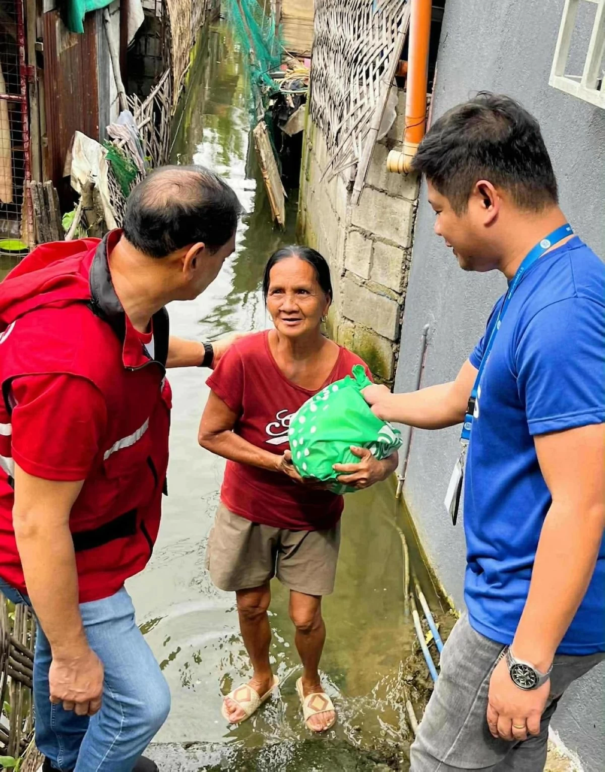 An SM employee-volunteer, along with a social good partner, navigate flooded alleys in Pampanga to personally hand a Kalinga Pack to a resident.