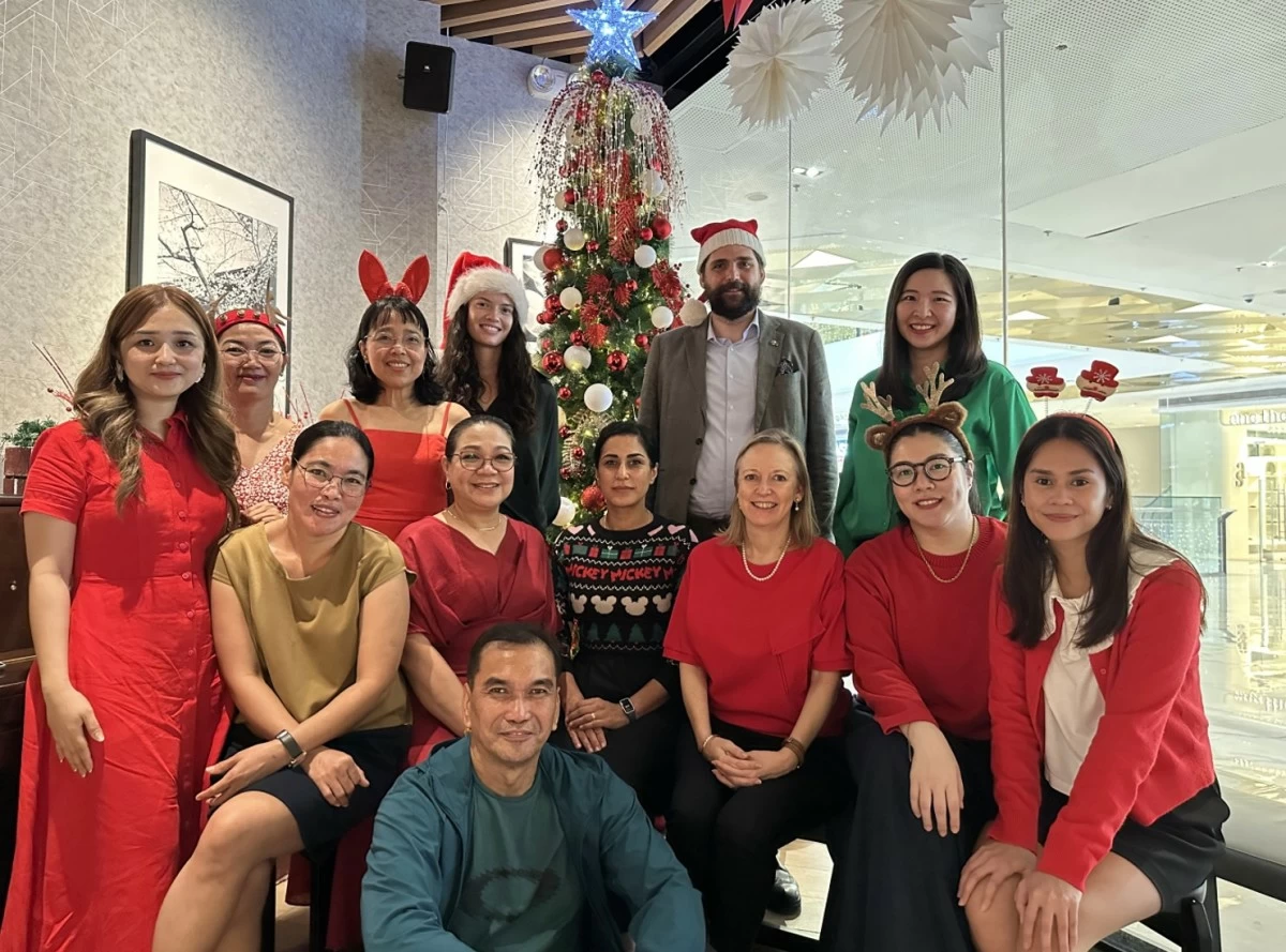 Ambassador Anna Ferry seated, (3rd from right) celebrates the holidays sharing joy and goodwill, with her embassy team—her source of cheer and success.