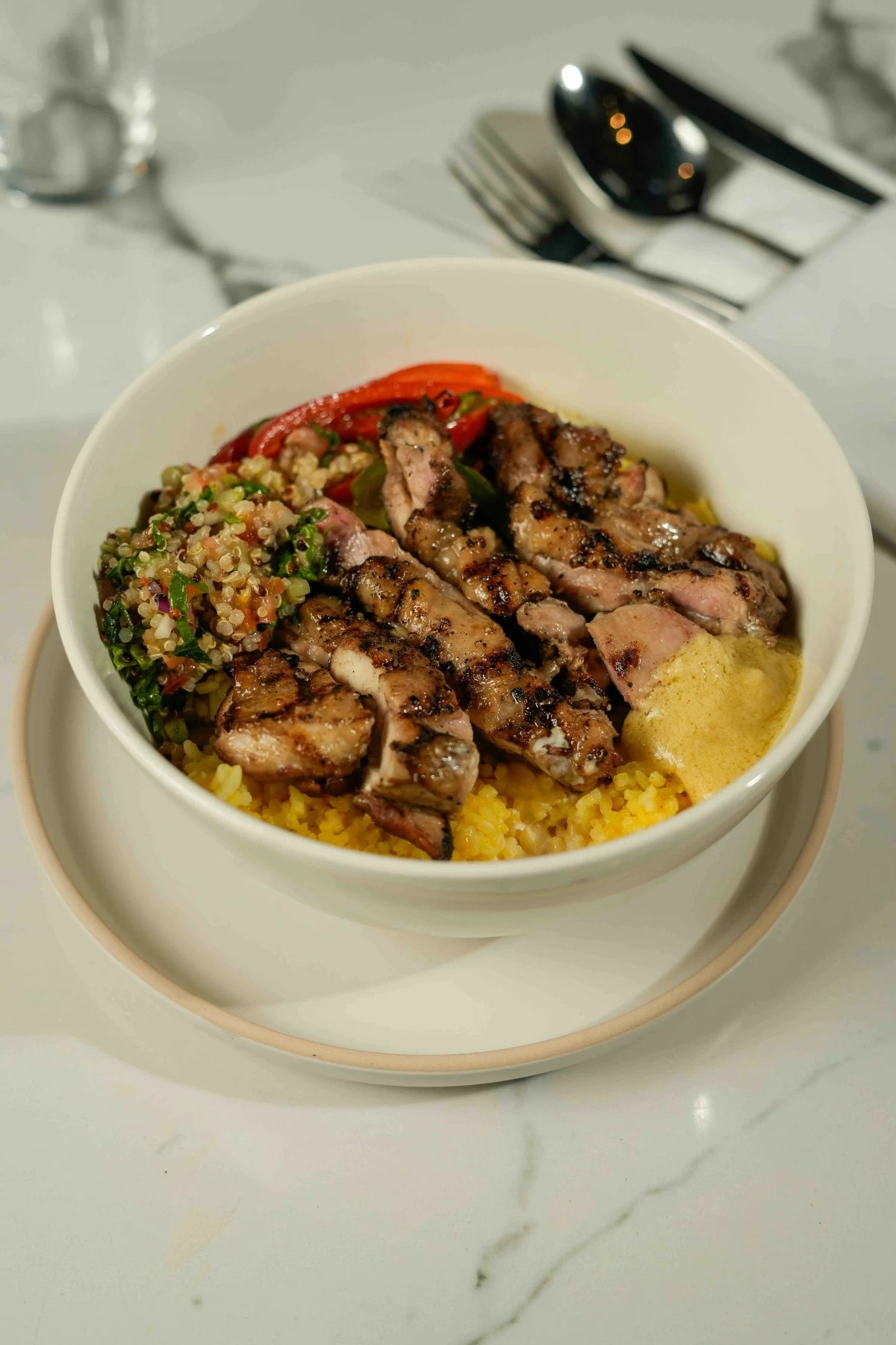 BALANCED BOWL Grilled chicken served with a quinoa mix, pickled vegetables, spiced chicken, turmeric rice, roasted egg, hummus and yogurt.