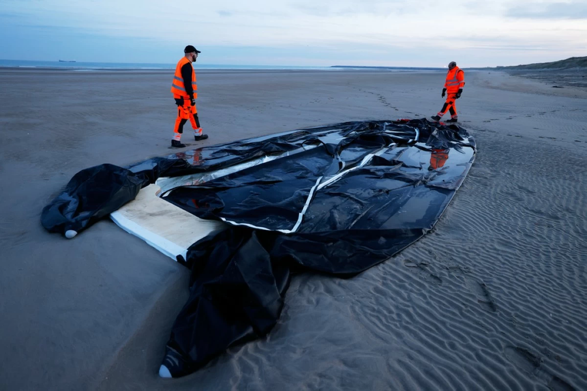 File - Town employees walk next to an inflatable boat punctured by French police and used by migrants to cross the Channel, Monday, Dec. 22, 2025 on the beach of Gravelines, northern France. (AP Photo/Jean-Francois Badias, File)