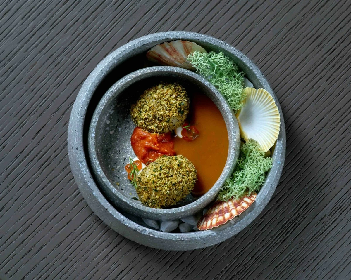 SWEET DEPTHS Butter-poached Hokkaido scallop with herb crust, sun-dried tomato, and crustacean bisque, balancing richness with delicate sweetness.