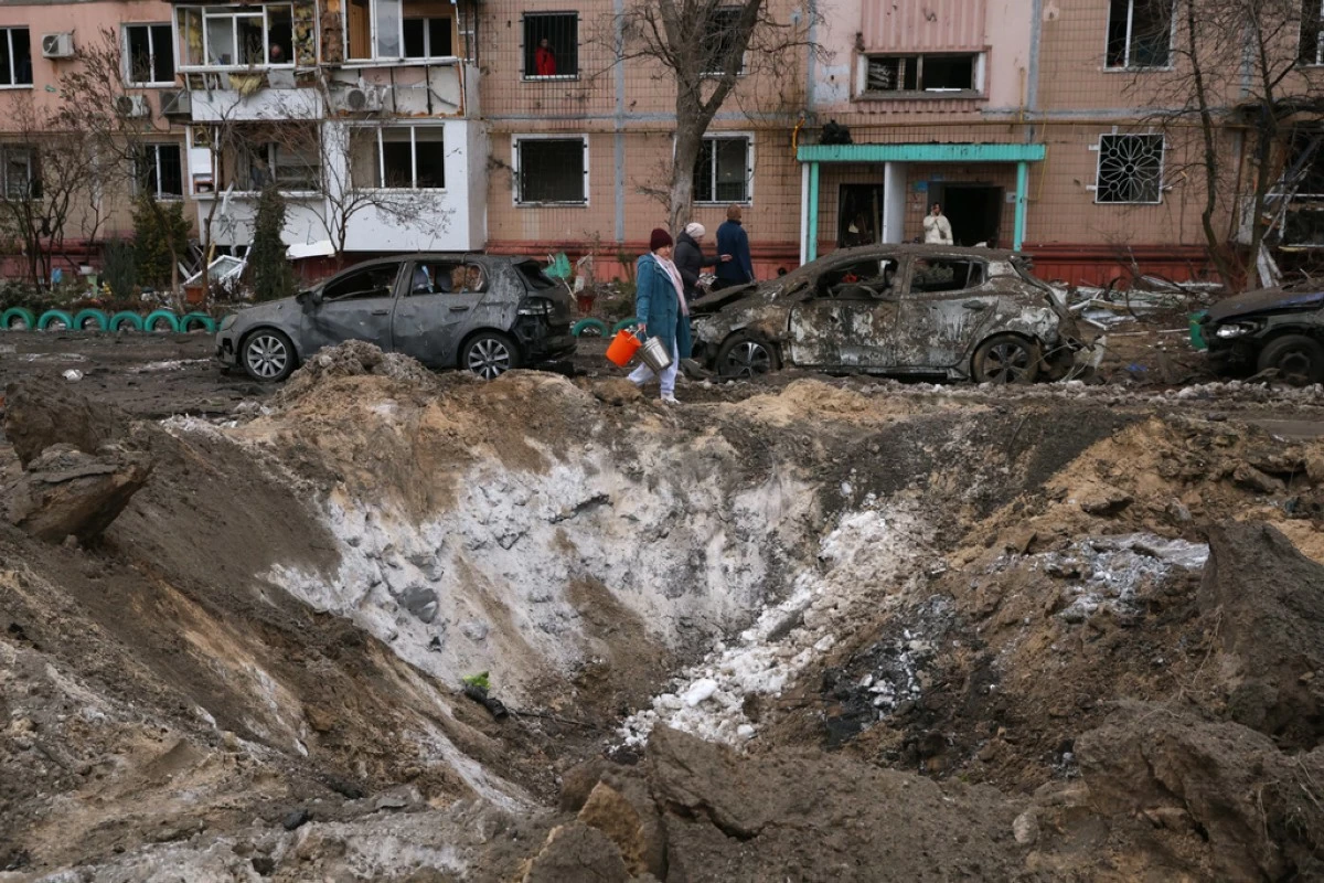 People pass a crater and damaged cars near an apartment building after a Russian attack in Zaporizhzhia, Ukraine, Wednesday, Jan. 28, 2026. (AP Photo/Kateryna Klochko)