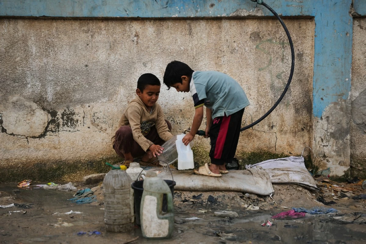 Palestinian children fill plastic bottles with water at a tent camp in Deir al-Balah, Gaza Strip, Thursday, Jan. 29, 2026. (AP Photo/Abdel Kareem Hana)