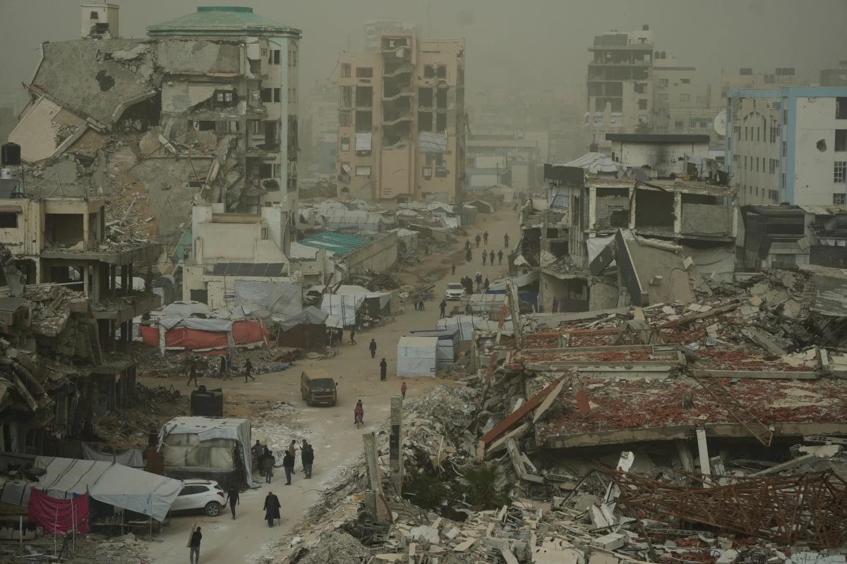 Palestinians walk along a street surrounded by buildings destroyed in Israeli air and ground operations during a dust storm in Gaza City, Saturday, Feb. 14, 2026. (AP Photo/Jehad Alshrafi)