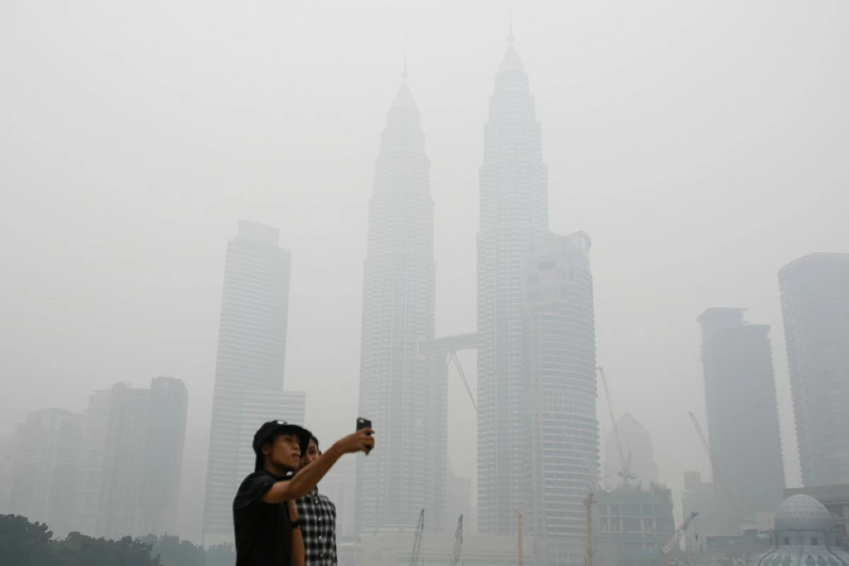 FILE -Tourists take a selfie against Malaysia's landmark building Petronas Twin Towers shrouded with haze in Kuala Lumpur, Malaysia on Sept. 26, 2015. (AP Photo/Joshua Paul, File)