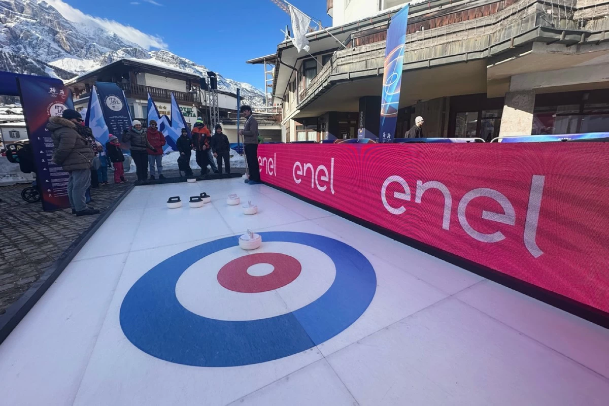 Olympic fans try curling next to signage for Enel at the fan village, during the 2026 Winter Olympics, in Cortina d'Ampezzo, Italy, Feb. 20, 2026. (AP Photo/ Jennifer McDermott)