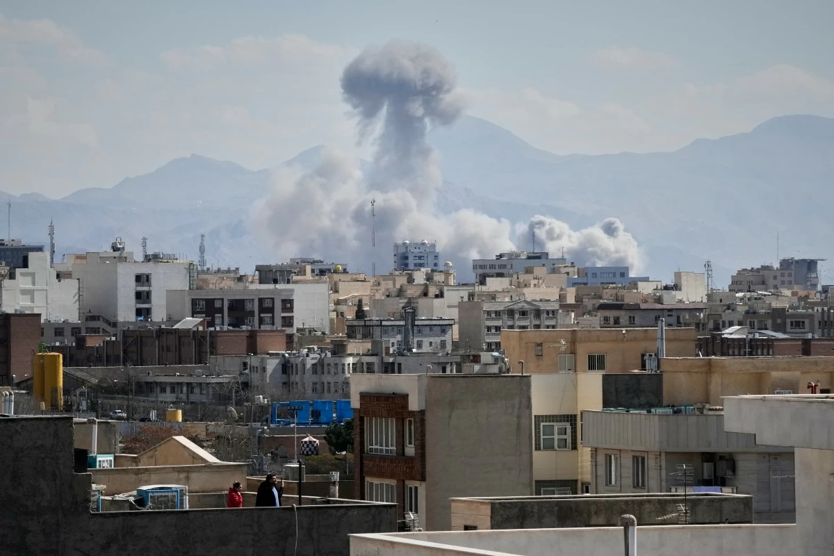 PEOPLE watch from a rooftop as a plume of smoke rises after a strike in Tehran, Iran, Sunday, March 1, 2026. (AP)