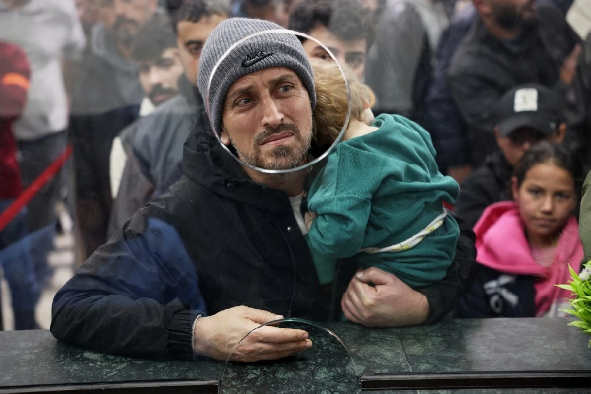 A Syrian man carries a child as they cross the Syrian-Lebanese border into Syria, fleeing Lebanon due to Israeli airstrikes, in Jdeidet Yabous, Syria, Tuesday, March 3, 2026. (AP Photo/Ghaith Alsayed)