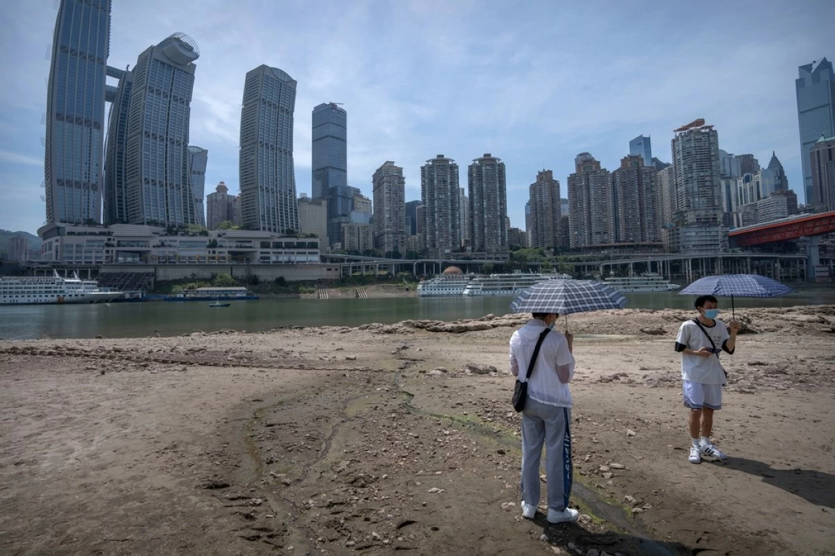 FILE - Students carrying umbrellas stand on the dry riverbed of the Jialing Rivera, a tributary of the Yangtze, in southwestern China's Chongqing Municipality, Aug. 19, 2022. (AP Photo/Mark Schiefelbein, File)