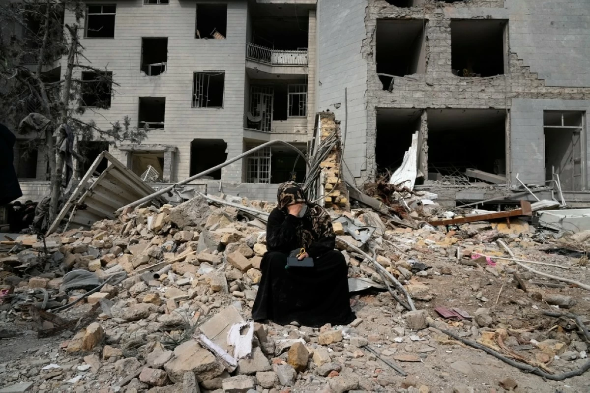 A woman sits on rubble across from a residential building damaged last Sunday during the U.S.-Israeli air campaign in Tehran, Iran, Thursday, March 12, 2026. (AP Photo/Vahid Salemi)