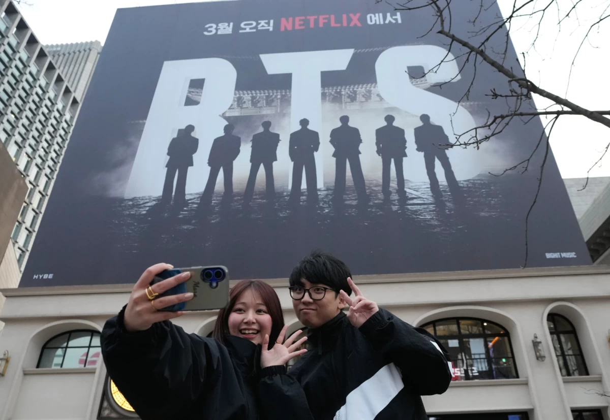 A couple takes a selfie near a banner promoting the K-pop group BTS's comeback concert at Gwanghwamun Square in Seoul on March 18. (AP)