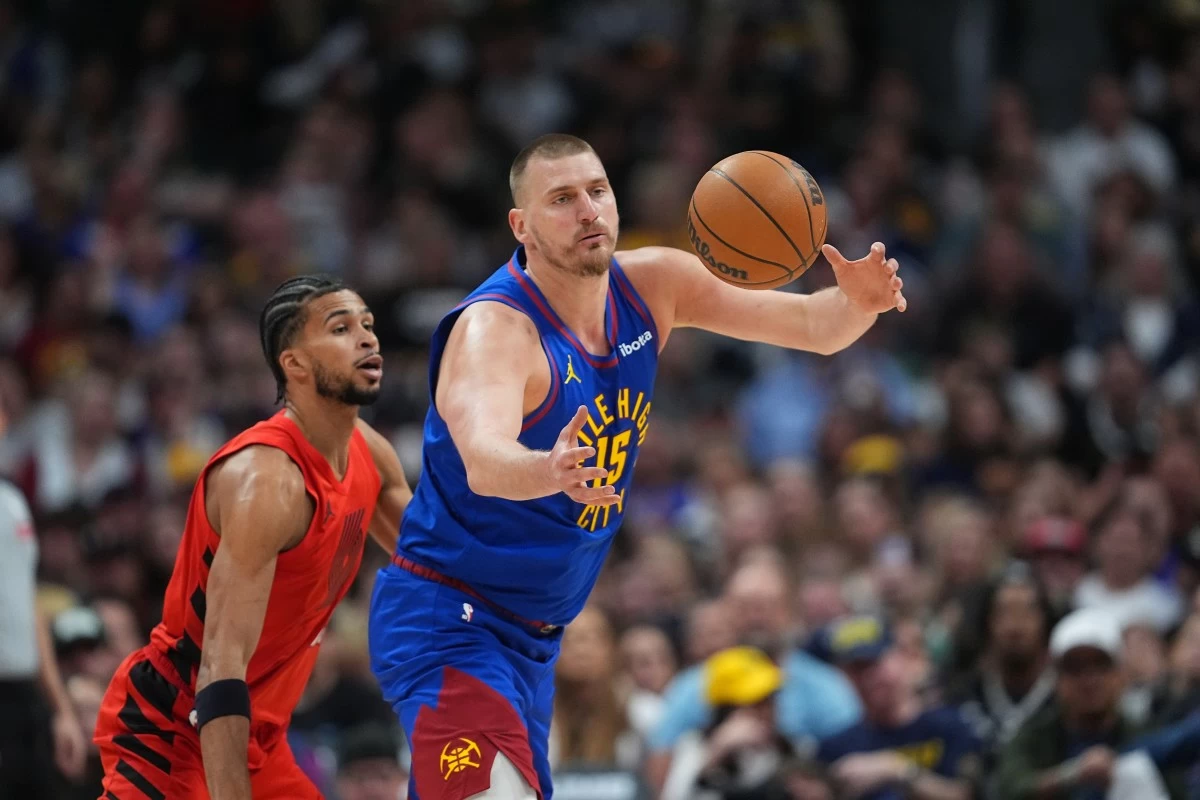 Denver Nuggets center Nikola Jokic, front, juggles the ball as Portland Trail Blazers forward Toumani Camara, left, defends in the first half of an NBA basketball game Sunday, March 22, 2026, in Denver. (AP Photo/David Zalubowski)