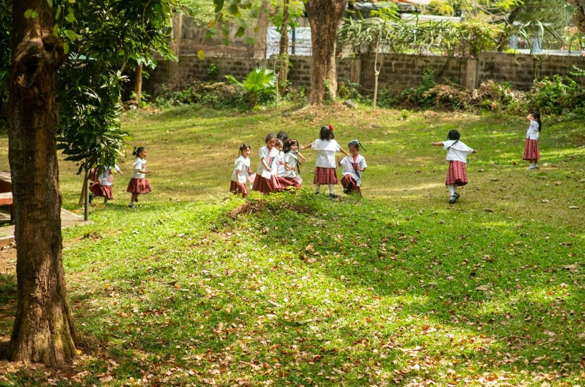 Grade school students run and play in an open campus space.