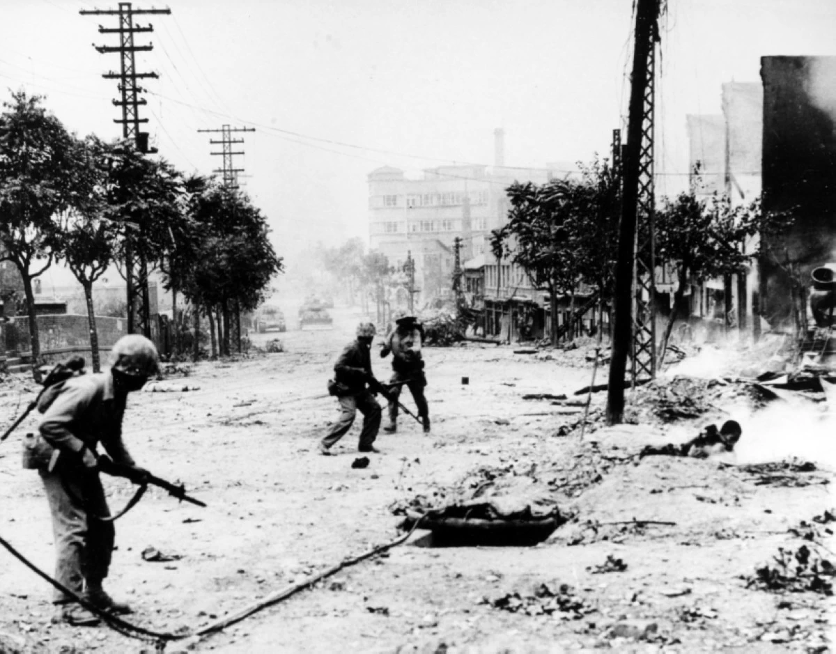 US Marines engaging in street fighting during the liberation of Seoul, circa late September 1950. Note M-1 rifles and Browning Automatic Rifles carried by the Marines, dead Koreans in the street, and M-4 Sherman tanks in the distance (Photo: US Naval History and Heritage Command)
